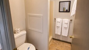 Ein kleines, sauberes Badezimmer mit Toilette, einem Handtuchhalter mit zwei Handtüchern, einem gerahmten Spiegel und einer Tür mit einem daran hängenden Handtuch.