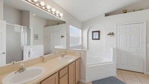 Une salle de bain avec deux lavabos, un grand miroir avec éclairage, une baignoire et une fenêtre.
