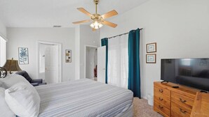 Une chambre à coucher avec un lit, un ventilateur de plafond, une télévision et une commode.