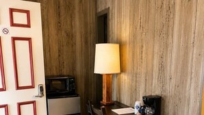 Ett kompakt kök med mikrovågsugn, kylskåp och ett träbord med en lampa.
