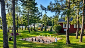 A chessboard set up on a grassy lawn surrounded by trees and a red building. - Pet Friendly Room 23-2 Queen Suite-Woodland Motor Lodge (Grayling)