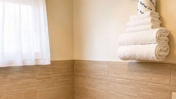 A modern bathroom with a toilet, a towel rack with folded towels, a toilet paper holder, and a heater under the sink.