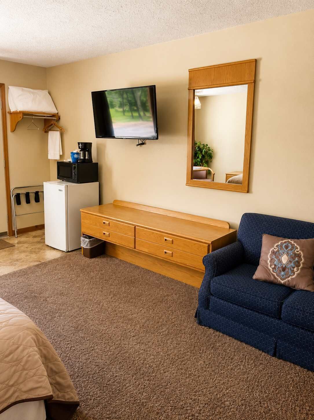 Een hotelkamer met een televisie, een houten kastje, een bank, een kleine koelkast en een spiegel.