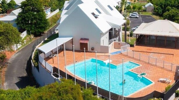 A modern building with a pool, surrounded by greenery and a view of the ocean. - Brand-new studio apartment, ocean view, pool, near beaches (Le Gosier)