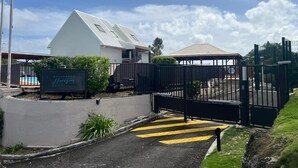 A gated entrance with a sign, a white building, and a fenced area with a pool. - Brand-new studio apartment, ocean view, pool, near beaches (Le Gosier)