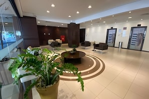 Um lobby moderno com área de estar central, balcão de recepção e uma grande planta em vaso.