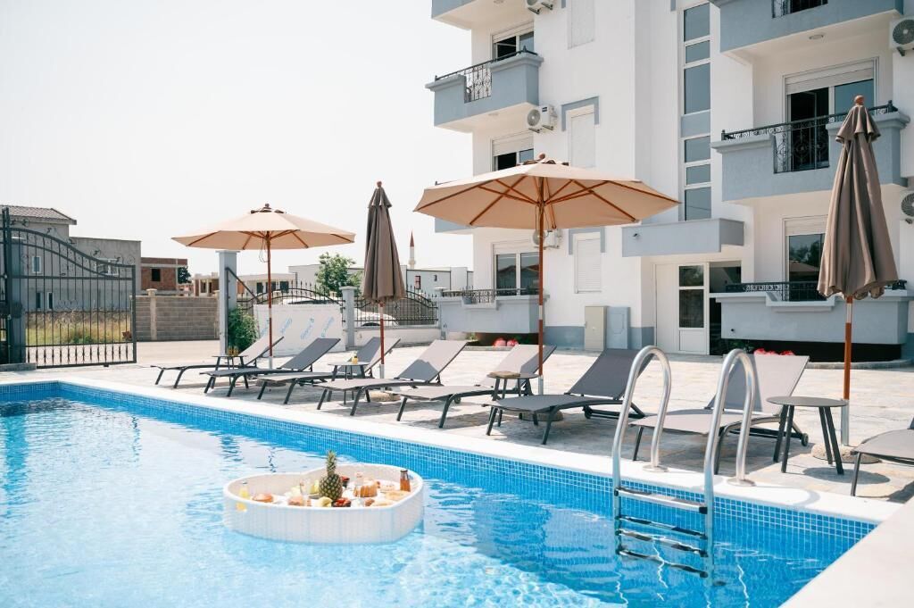 A swimming pool with lounge chairs and umbrellas, surrounded by a modern building with balconies.