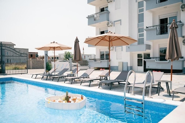 A swimming pool with lounge chairs and umbrellas, surrounded by a modern building with balconies.