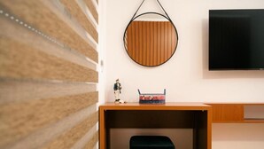 Ein modernes Zimmer mit einem Holztisch, einem runden Spiegel, einem schwarzen Stuhl und einem an der Wand befestigten Flachbildfernseher.