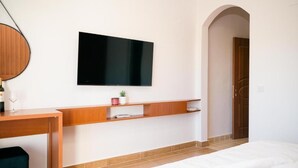 Ein modernes Hotelzimmer mit Wand-Fernseher, einem Holztisch mit Weinglas, einer kleinen Topfpflanze und einem Bett mit weißer Bettwäsche.