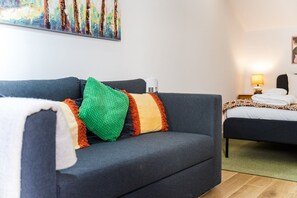 A modern hotel room with a grey sofa, colorful cushions, a bed with a patterned bedspread, a bedside table with a lamp, and a painting on the wall. - GuestReady-Charming Studio in Funchal's Heart (Funchal)