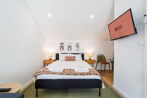 A hotel room with a bed, two bedside tables with lamps, a chair, a TV, and artwork on the wall. - GuestReady-Charming Studio in Funchal's Heart (Funchal)