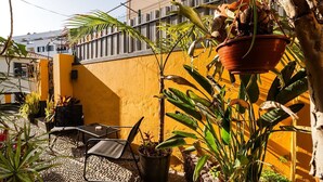 En terrasse med et bord og stole, omgivet af plantekasser og en gul væg.
