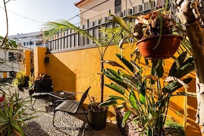 A patio with a table and chairs, surrounded by potted plants and a yellow wall. - GuestReady-Charming Studio in Funchal's Heart (Funchal)