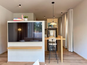Eine moderne Küche mit Einbauofen, eine Essecke mit Holztisch und -stühlen sowie ein großes Fenster mit Vorhängen.