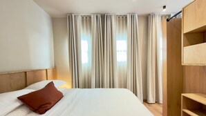Ett hotellrum med en stor säng, en sänggavel i trä, en garderob och ett fönster med gardiner.