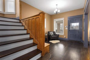 A staircase with wooden steps and a handrail, a dark grey door, and a window with blinds. - Large Home_Sleeps 9_Near Plaza, Dogs Ok (Kansas City)