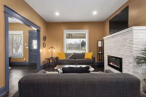A living room with a fireplace, a sofa, a coffee table, and a window with blinds. - Large Home_Sleeps 9_Near Plaza, Dogs Ok (Kansas City)