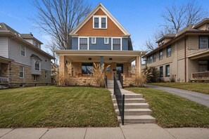 A two-story house with a front porch, a stone foundation, and a clear sky. - Large Home_Sleeps 9_Near Plaza, Dogs Ok (Kansas City)