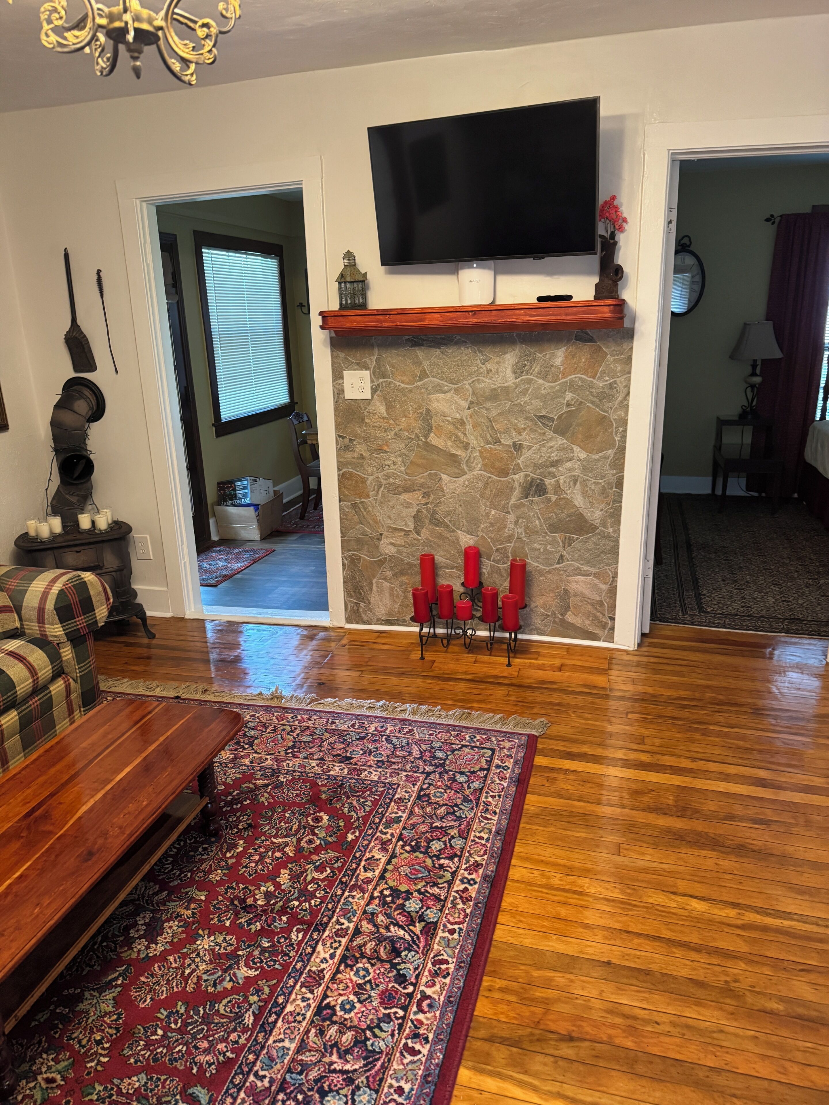 A living room with a stone fireplace, a flat-screen TV mounted above it, a plaid sofa, a wooden coffee table, and a patterned rug.