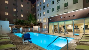 A hotel pool area with lounge chairs and a fitness center visible through the glass doors. - ADA Queen Studio w/ Tub | Free Breakfast! (Miami)
