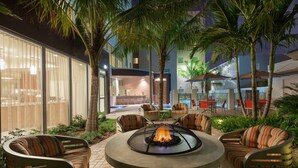 An outdoor patio area with a fire pit, seating, and a view of the building's interior. - ADA Queen Studio w/ Tub | Free Breakfast! (Miami)