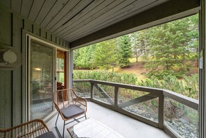 Eine überdachte Veranda mit Korbstühlen, eine Glastür, die zu einem Raum führt, und Blick auf eine bewaldete Landschaft.