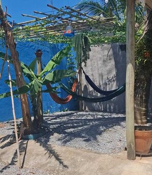 Eine Hängematte, die zwischen zwei Holzpfosten gespannt ist, mit einer blauen Wand und einem Blumentopf im Hintergrund.