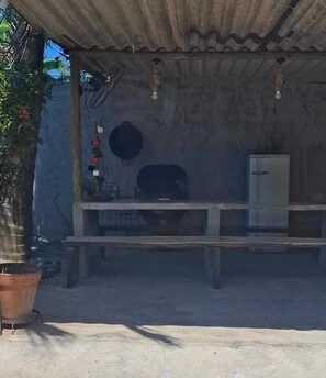 Ein überdachter Außenbereich mit einer Betonbank, einem Metallschrank und einem Blumentopf.