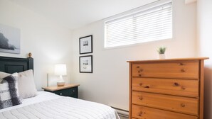 A bedroom with a bed, a dresser, a nightstand, a lamp, and framed pictures on the wall. - SKI-IN/SKI-OUT 1BDR Condo with Pool & Hot Tub | Spectacular location! (Whistler)