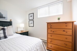 A bedroom with a bed, a dresser, a nightstand, a lamp, and framed pictures on the wall. - SKI-IN/SKI-OUT 1BDR Condo with Pool & Hot Tub | Spectacular location! (Whistler)