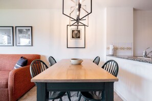 A dining area with a wooden table, chairs, a bowl, framed pictures on the wall, and a kitchen in the background. - SKI-IN/SKI-OUT 1BDR Condo with Pool & Hot Tub | Spectacular location! (Whistler)