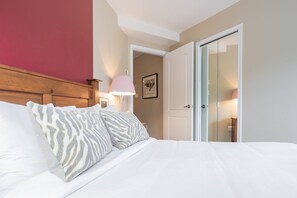 Et hotelværelse med en seng, et træhovedgærde, en dør, en væglampe og et indrammet billede.