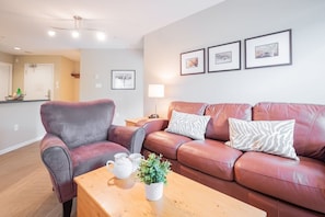 A living room with a leather sofa, a wooden coffee table, and a small plant. There are framed pictures on the wall and a kitchen area in the background. - Pet friendly condo on Whistler Village stroll (Whistler)