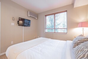 A bedroom with a bed, a television, an air conditioning unit, a window with blinds, and a lamp. - Pet friendly condo on Whistler Village stroll (Whistler)