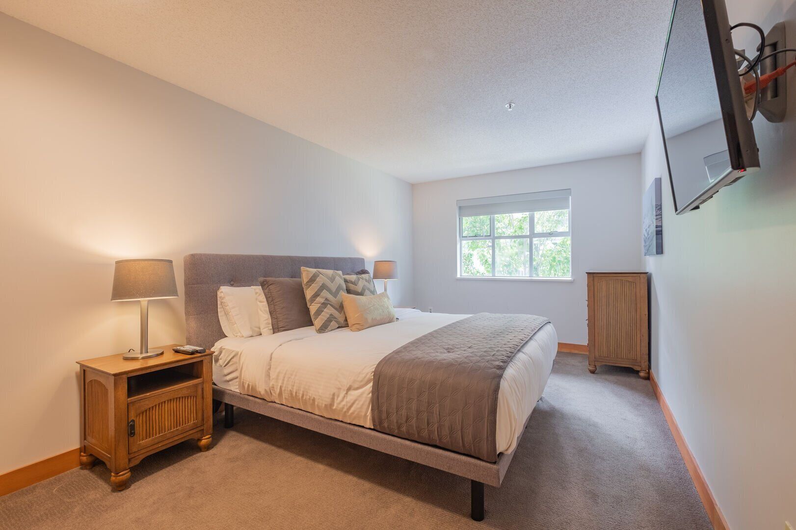A bedroom with a bed, bedside tables, a window, and a TV mounted on the wall.