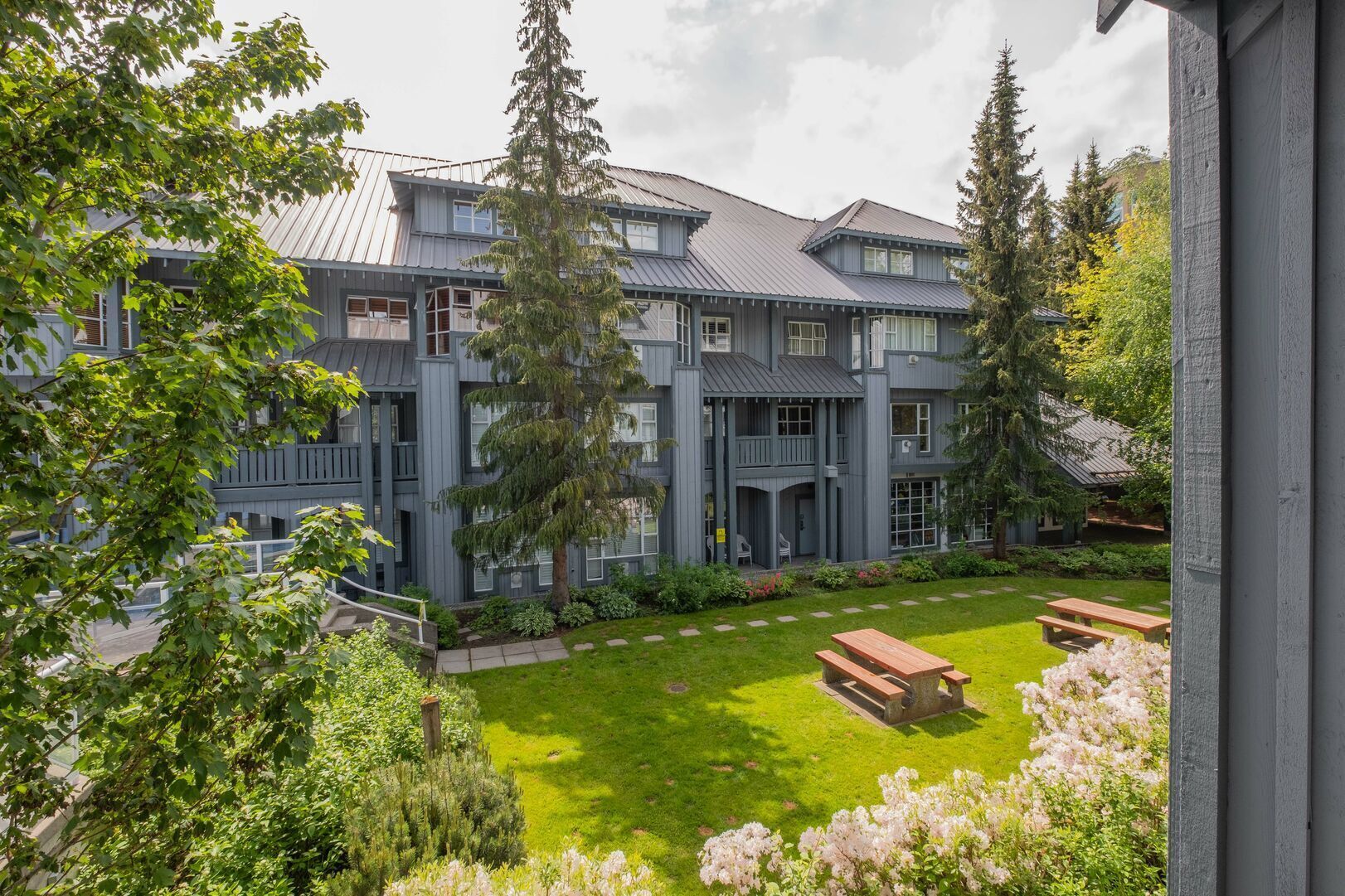 Un edificio de varios pisos con un patio interior, que incluye un área verde con bancos y una mesa de picnic.