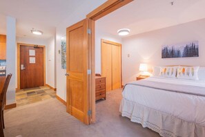 Une chambre à coucher avec un lit, une table de chevet, une lampe, un tableau accroché au mur et une porte en bois.