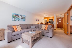 Ein Wohnzimmer mit einem grauen Ecksofa, einem Holztisch und einem Bild an der Wand.