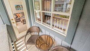 Eine Veranda mit Korbstühlen, einem Glastisch und Blick auf ein Haus durch ein Fenster.