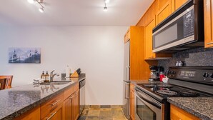 Eine moderne Küche mit Holzschränken, einer Granit-Arbeitsplatte, Edelstahlgeräten und einem gefliesten Boden.