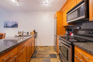 Eine moderne Küche mit Holzschränken, einer Granit-Arbeitsplatte, Edelstahlgeräten und einem gefliesten Boden.