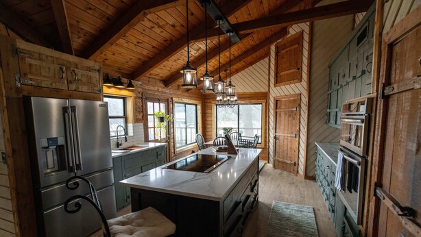 A spacious kitchen with wooden beams, a large island, stainless steel appliances, and hanging pendant lights.