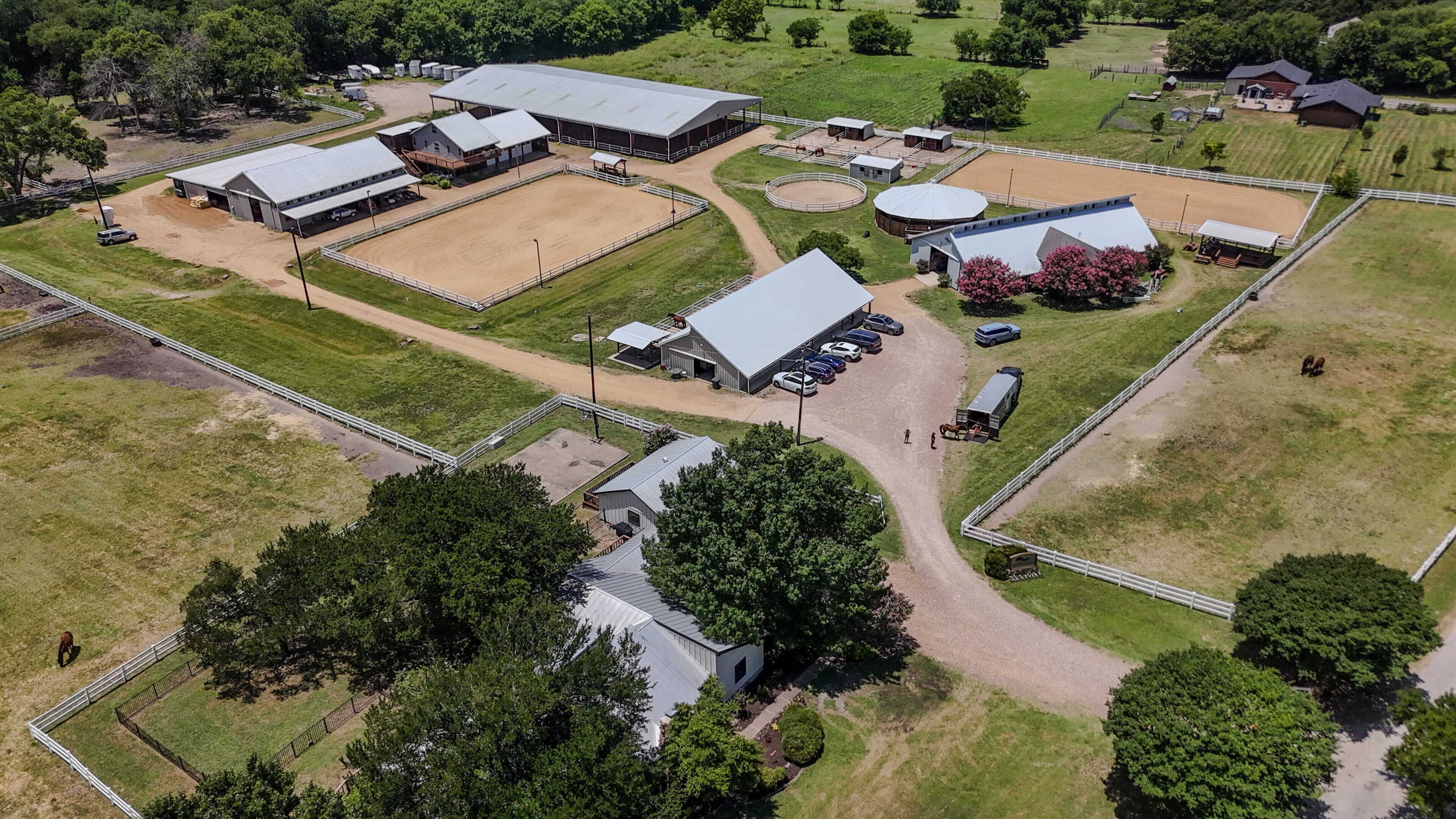 An aerial view of a large equestrian facility with multiple barns, riding arenas, and a central circular track.