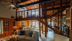 A spacious living area with a high ceiling, wooden beams, a staircase, and a dining area.