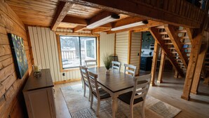 A wooden interior with a dining table, chairs, a small cabinet, and a staircase.
