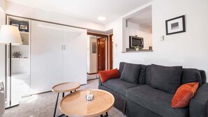 A modern living room with a grey sofa, two round wooden tables, and a white wardrobe. - Cozy Studio in the heart of Whistler | Walk to everything (Whistler)