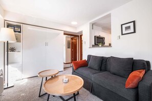 A modern living room with a grey sofa, two round wooden tables, and a white wardrobe. - Cozy Studio in the heart of Whistler | Walk to everything (Whistler)