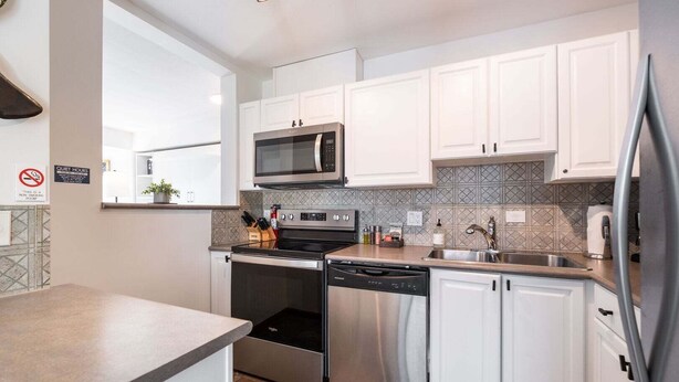 A modern kitchen with white cabinets, a stainless steel microwave, oven, and dishwasher, a tiled backsplash, and a sink with a faucet. - Cozy Studio in the heart of Whistler | Walk to everything (Whistler)