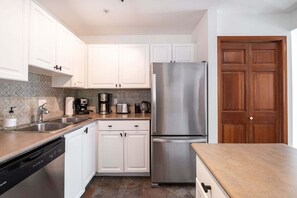 A modern kitchen with white cabinets, stainless steel appliances, and a wooden door. - Cozy Studio in the heart of Whistler | Walk to everything (Whistler)